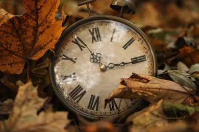 Photo of Autumn time. Vintage clock on fallen leaves in park, closeup