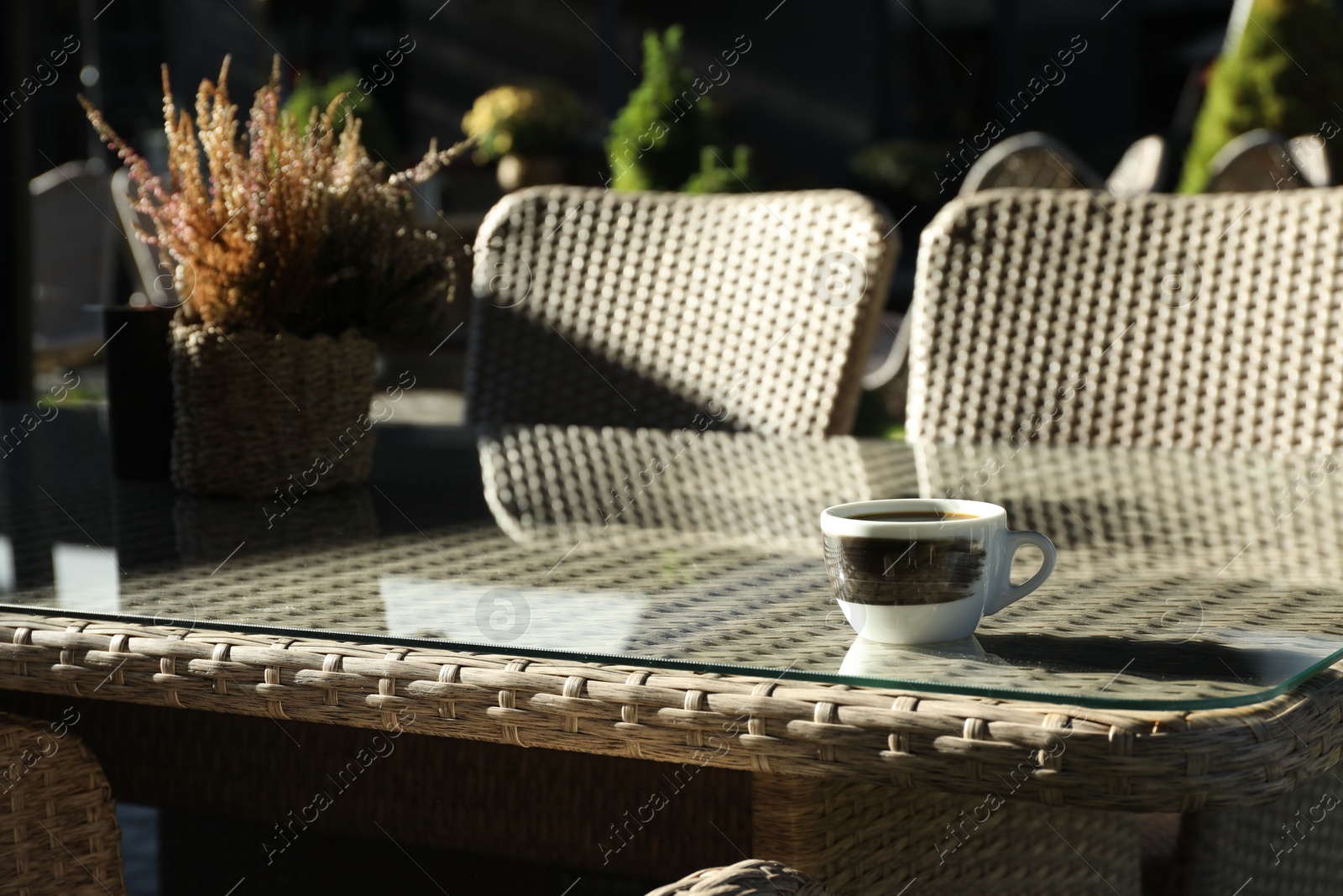 Photo of Table with cup of coffee, flowers and chairs in outdoor cafe, closeup