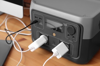 Photo of Portable power station with chargers on wooden desk indoors, closeup