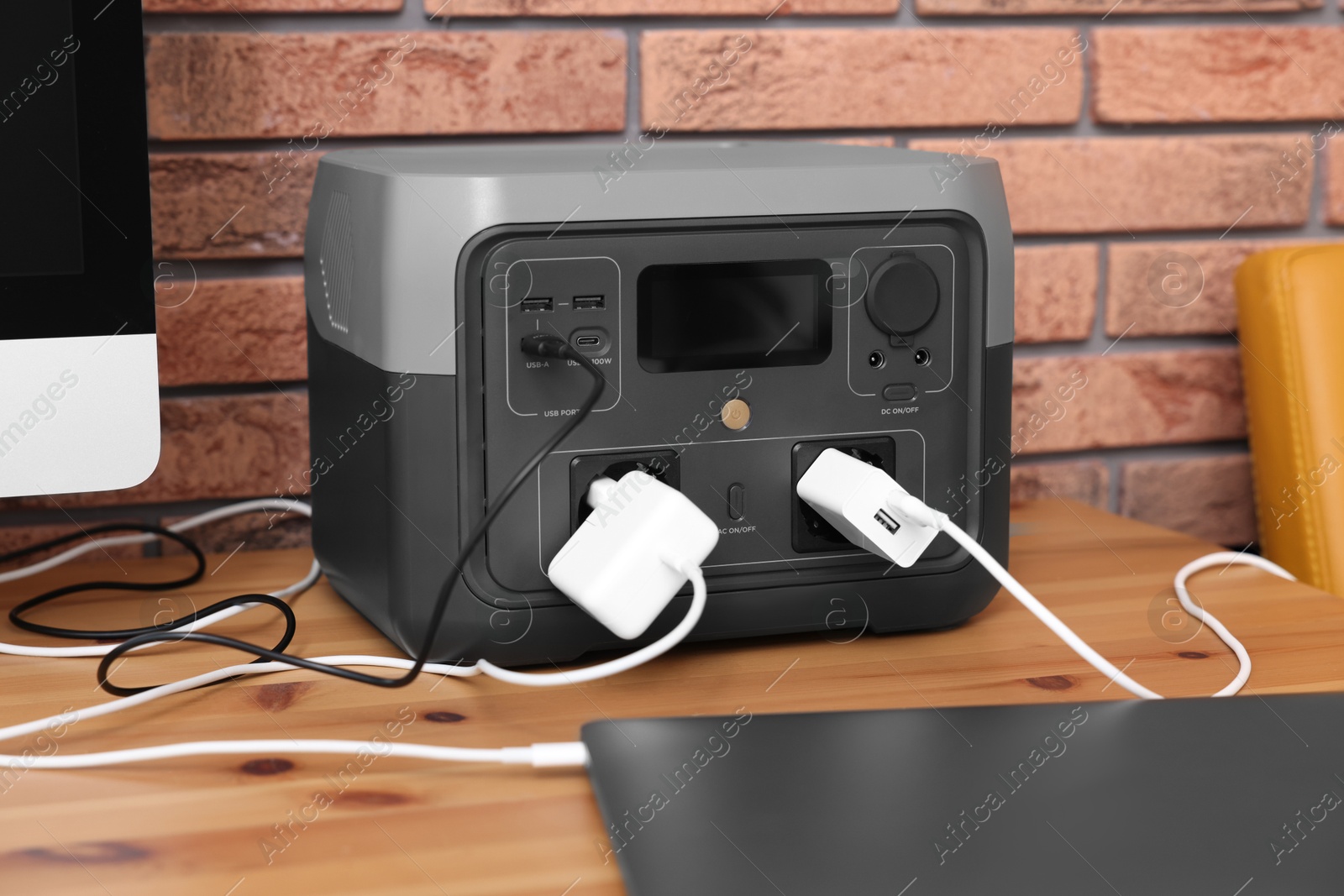 Photo of Laptop charging from portable power station on wooden desk indoors