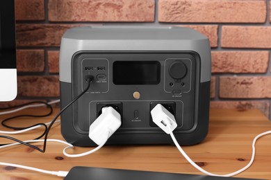 Photo of Portable power station with chargers on wooden desk indoors