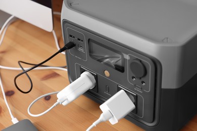 Photo of Portable power station with chargers on wooden desk indoors, closeup