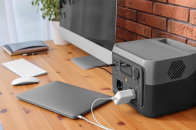 Photo of Devices charging from portable power station on wooden desk indoors