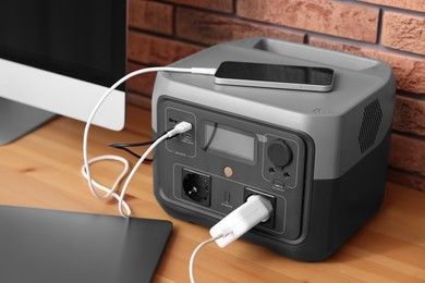 Photo of Devices charging from portable power station on wooden desk indoors