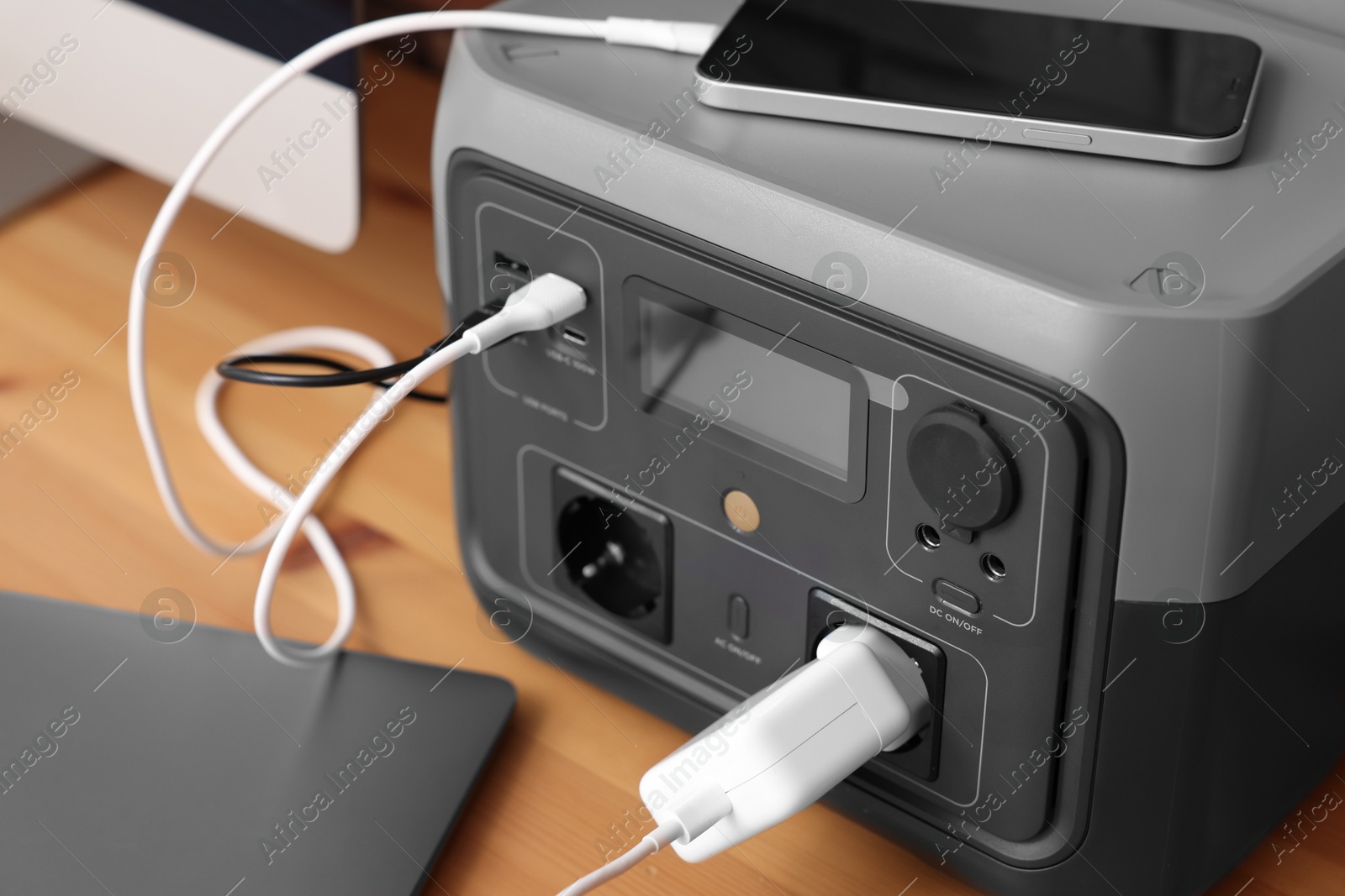 Photo of Devices charging from portable power station on wooden desk indoors, closeup