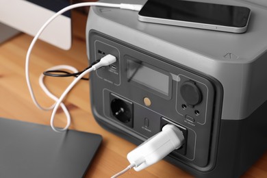 Photo of Devices charging from portable power station on wooden desk indoors, closeup