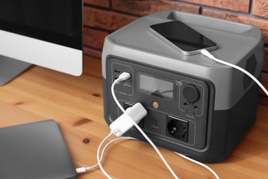 Photo of Devices charging from portable power station on wooden desk indoors