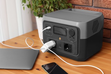 Photo of Devices charging from portable power station on wooden desk indoors