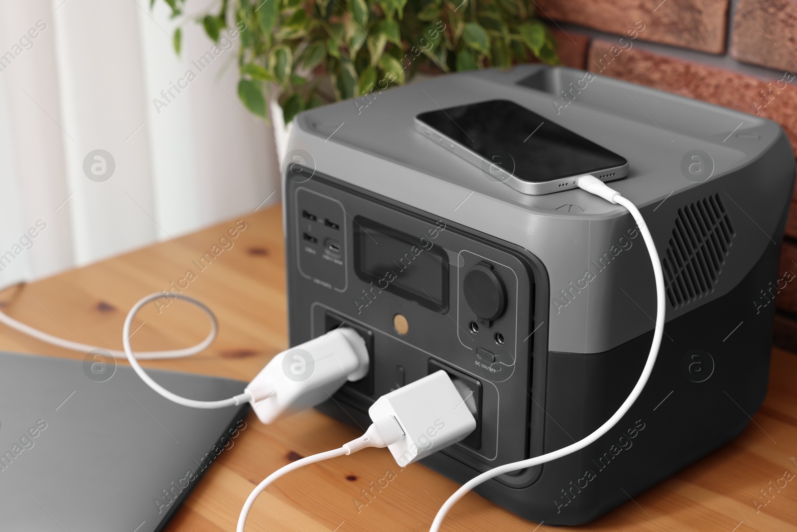 Photo of Devices charging from portable power station on wooden desk indoors