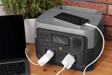 Photo of Devices charging from portable power station on wooden desk indoors