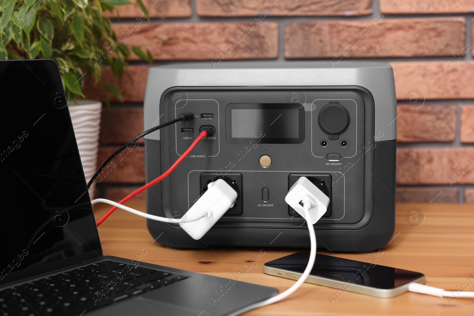 Photo of Devices charging from portable power station on wooden desk indoors