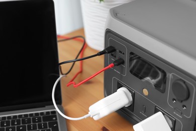 Photo of Laptop charging from portable power station on wooden desk indoors, closeup