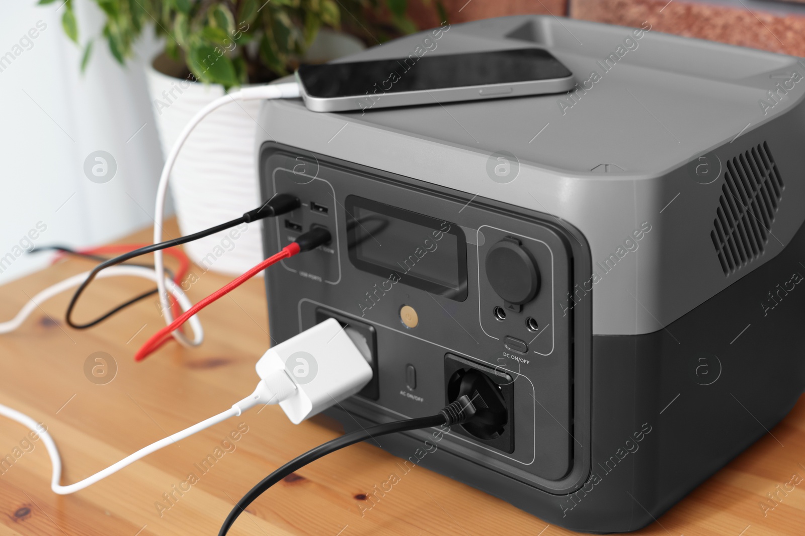 Photo of Smartphone charging from portable power station on wooden desk