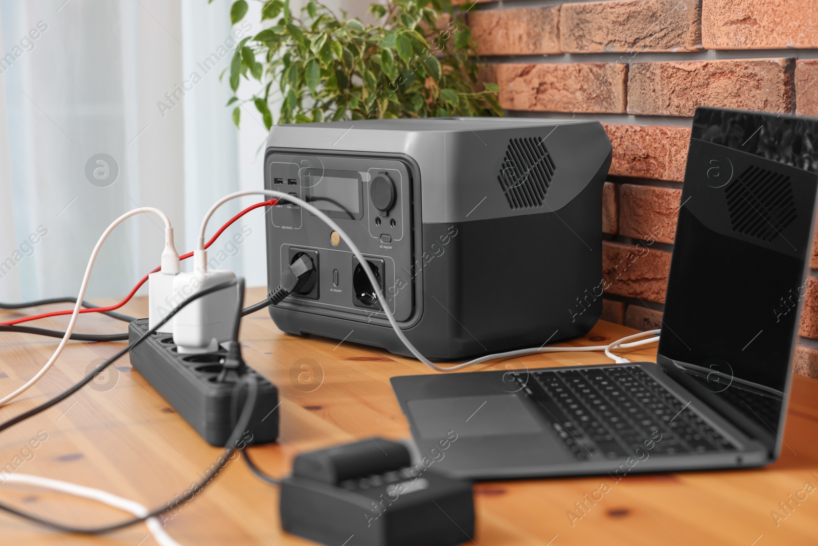 Photo of Laptop charging from portable power station on wooden desk indoors