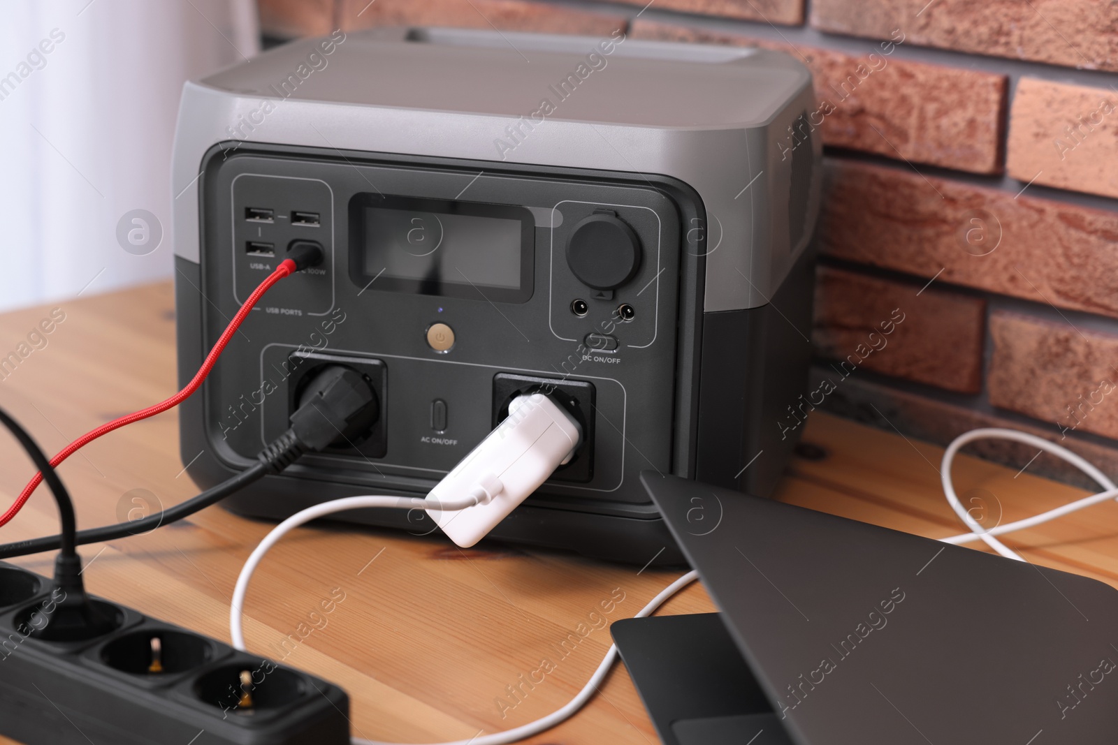 Photo of Laptop charging from portable power station on wooden desk indoors