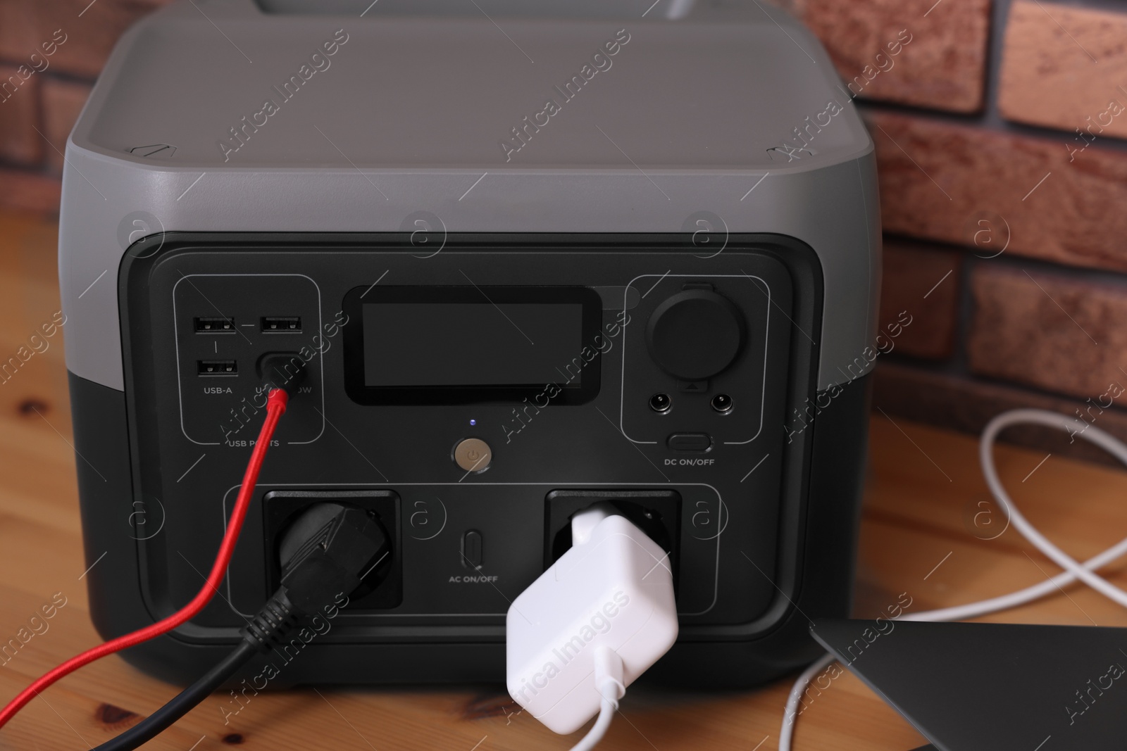 Photo of Portable power station with chargers on wooden desk indoors