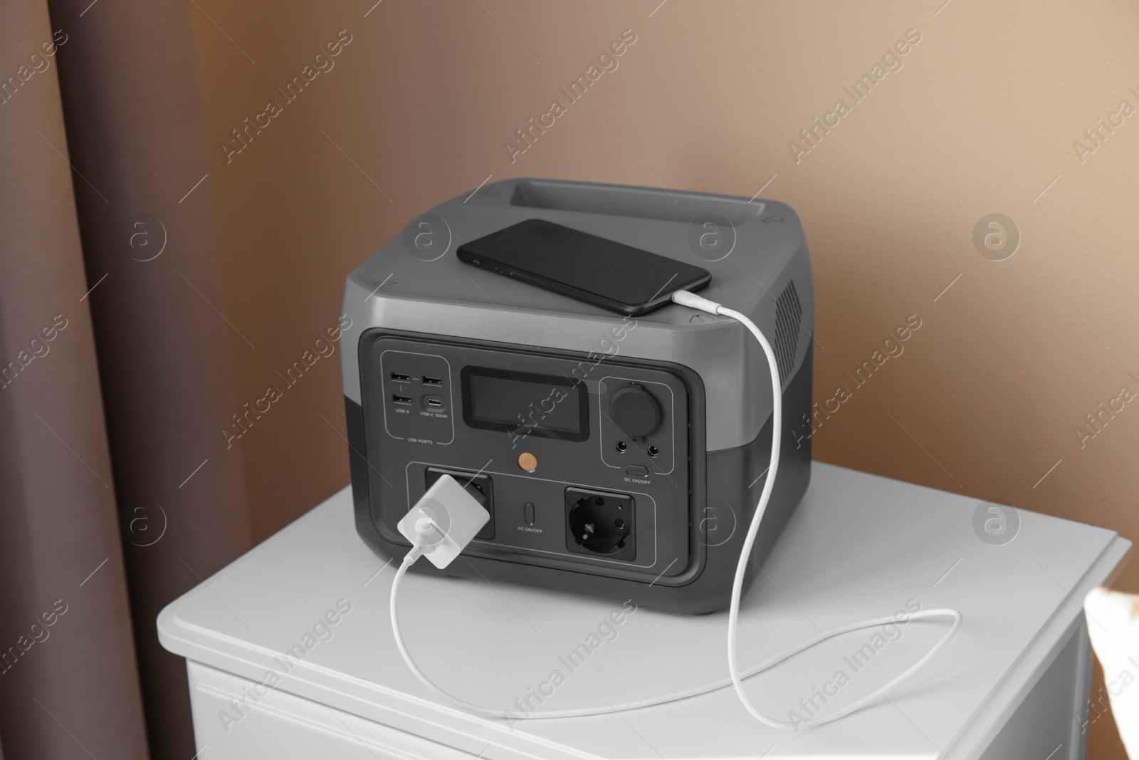 Photo of Smartphone charging from portable power station on nightstand indoors