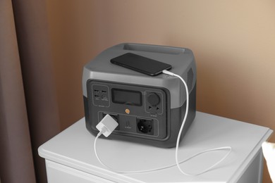 Photo of Smartphone charging from portable power station on nightstand indoors