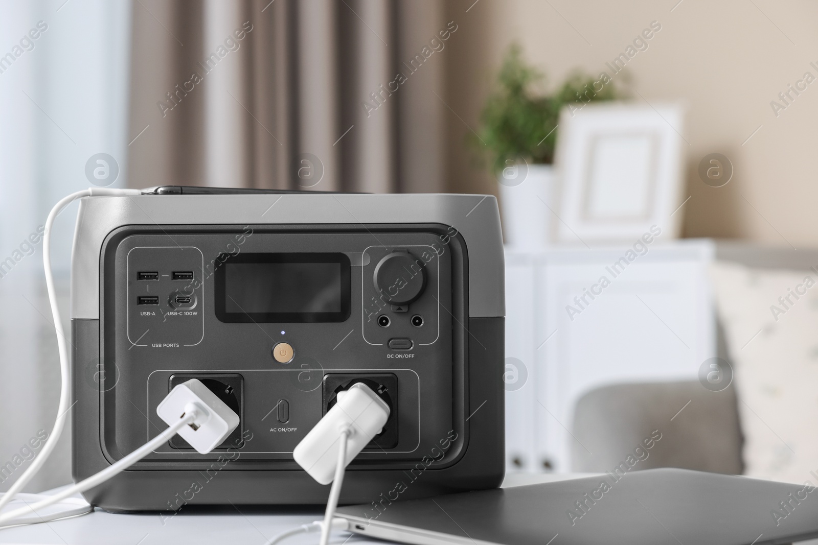 Photo of Devices charging from portable power station on white table indoors