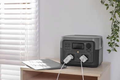 Photo of Laptop charging from portable power station on wooden table indoors