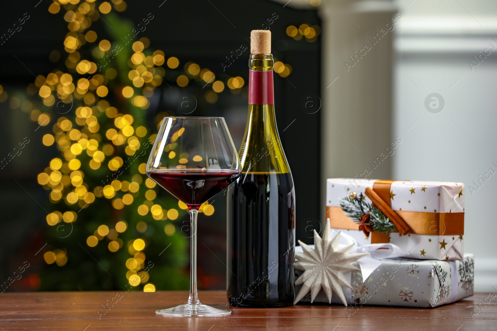 Photo of Red wine and gift boxes on wooden table against blurred Christmas lights. Bokeh effect