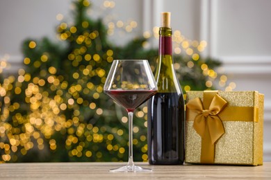 Photo of Red wine and gift box on wooden table against blurred Christmas lights, bokeh effect. Space for text