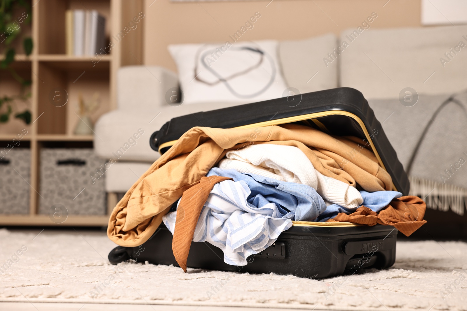 Photo of Open suitcase full of different messy clothes on floor indoors