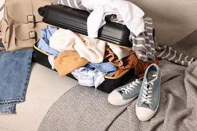 Photo of Open suitcase full of different messy clothes and sneakers on sofa indoors