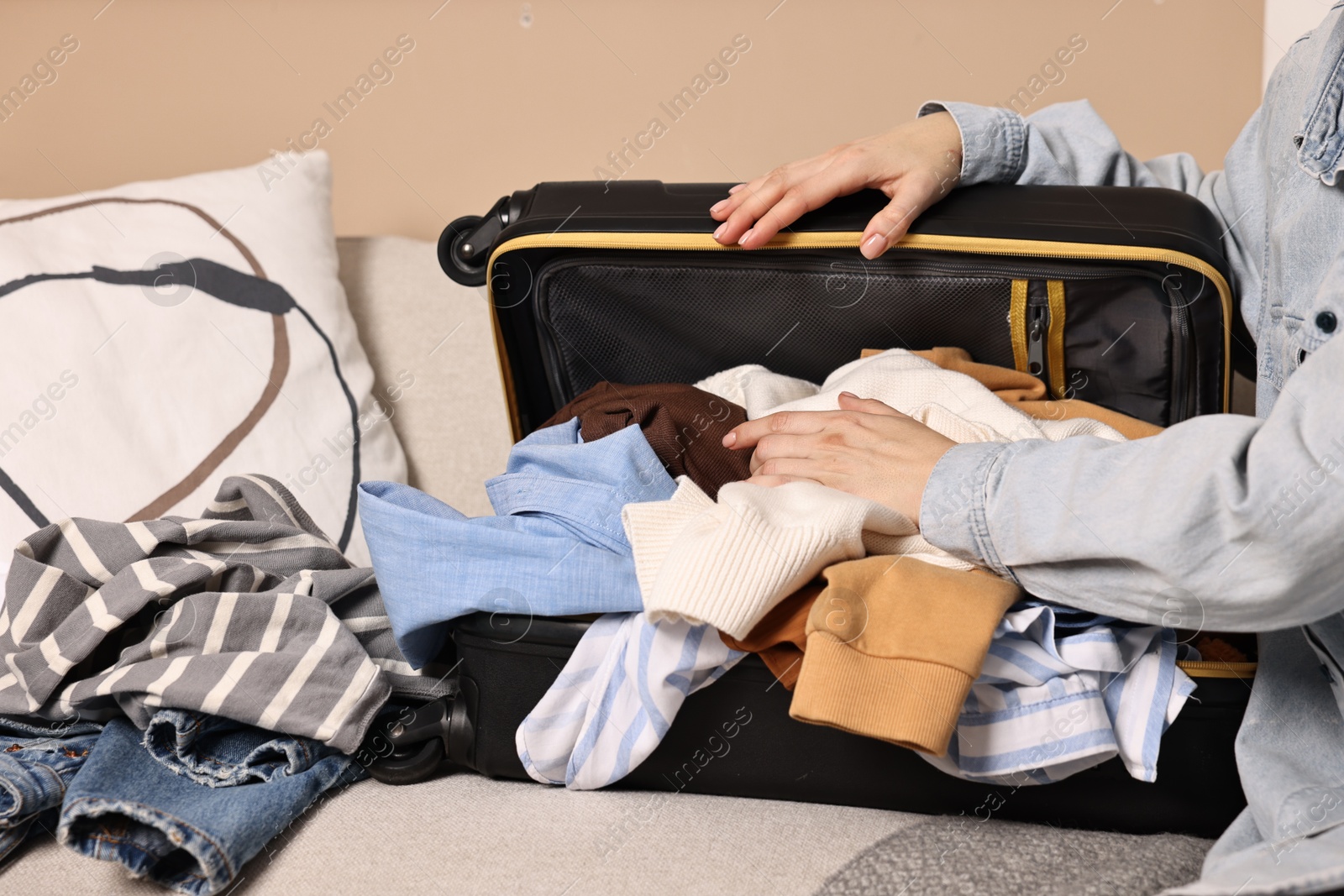 Photo of Woman packing different messy clothes into suitcase indoors, closeup