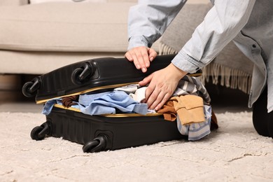 Photo of Woman trying to close suitcase full of different messy clothes indoors, closeup