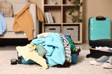 Photo of Suitcase with pile of different messy clothes on carpet