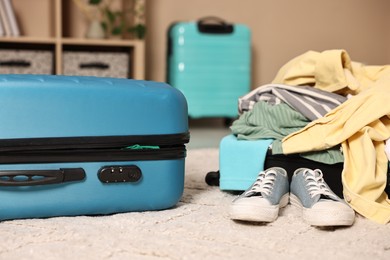 Photo of Suitcase with pile of different messy clothes, another one and sneakers on carpet