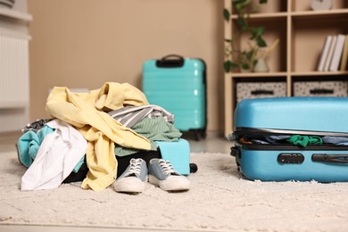 Photo of Suitcase with pile of different messy clothes, another one and sneakers on carpet