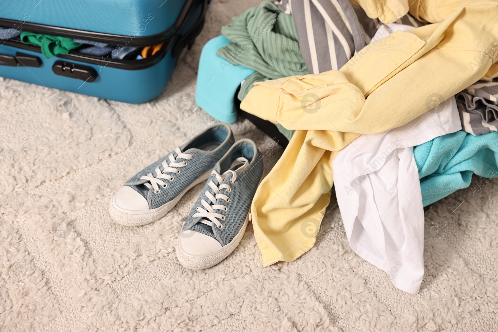 Suitcase with pile of different messy clothes, another one and sneakers on carpet Photo of Suitcase with pile of different messy clothes, another one and sneakers on carpet