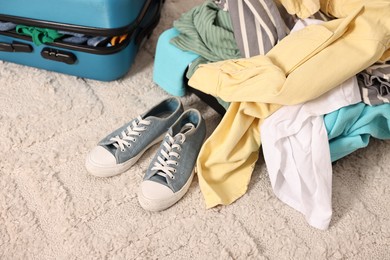 Photo of Suitcase with pile of different messy clothes, another one and sneakers on carpet