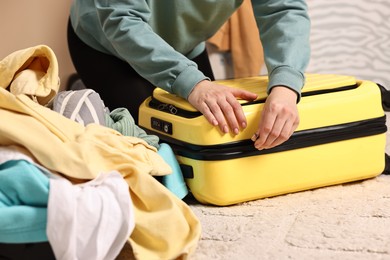 Photo of Woman closing suitcase near pile of different messy clothes indoors, closeup