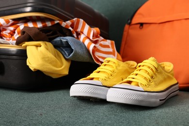 Photo of Suitcase full of different messy clothes and sneakers on sofa, closeup