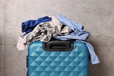 Photo of Suitcase and pile of different messy clothes near grey marble wall