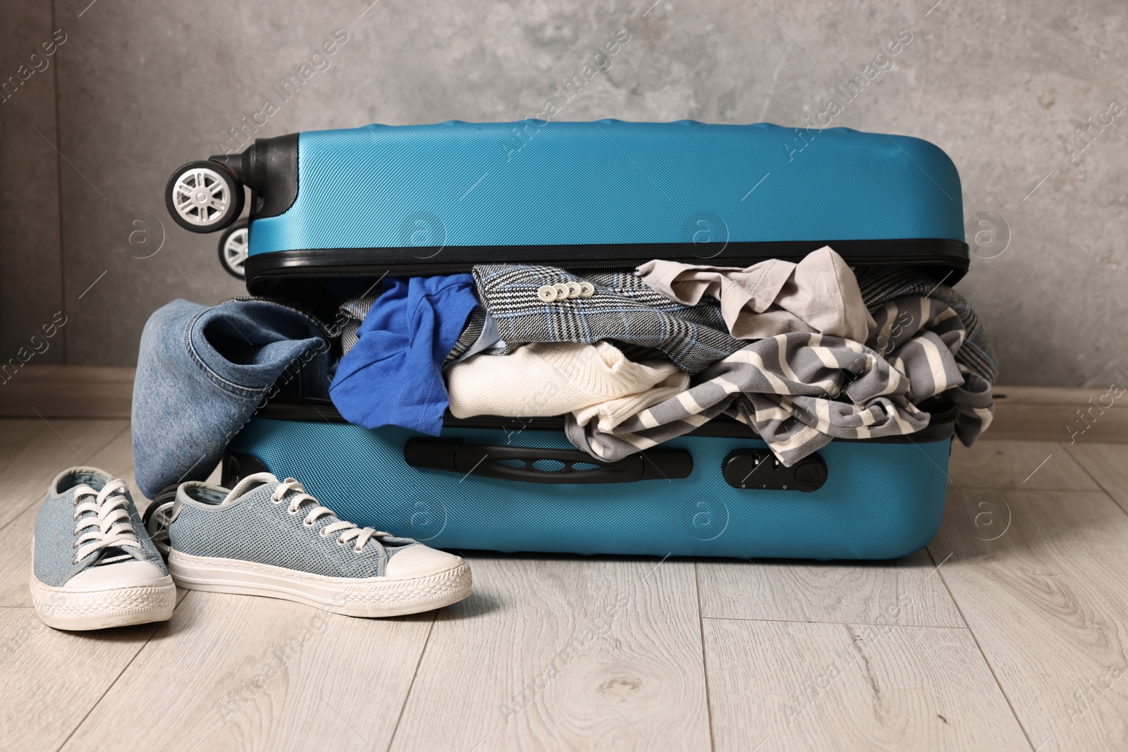 Photo of Open suitcase full of different messy clothes and sneakers on floor indoors