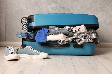 Photo of Open suitcase full of different messy clothes and sneakers on floor indoors