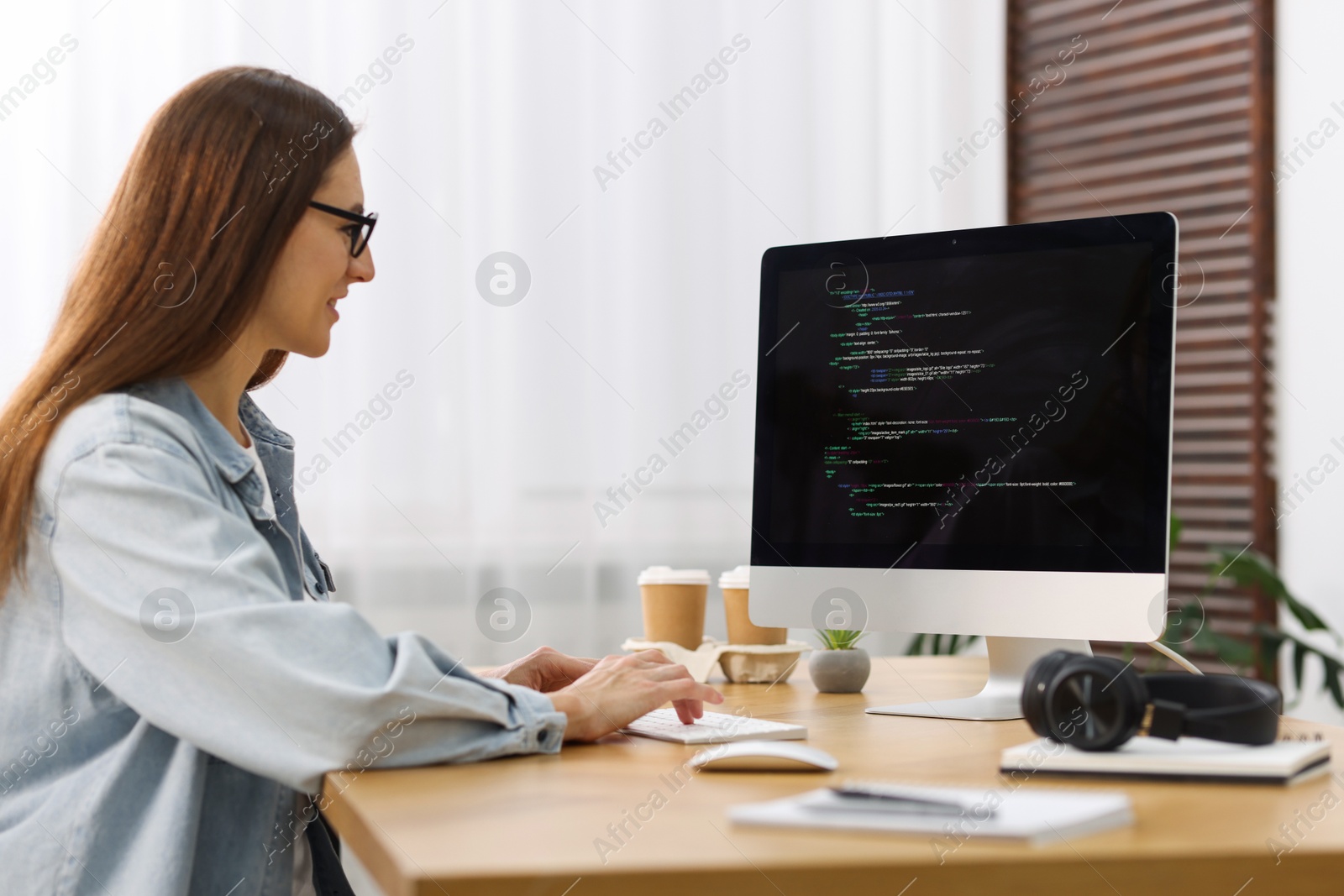 Photo of Programmer working on computer at wooden desk indoors