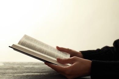 Photo of Woman with open Holy Bible in English language at wooden table, closeup