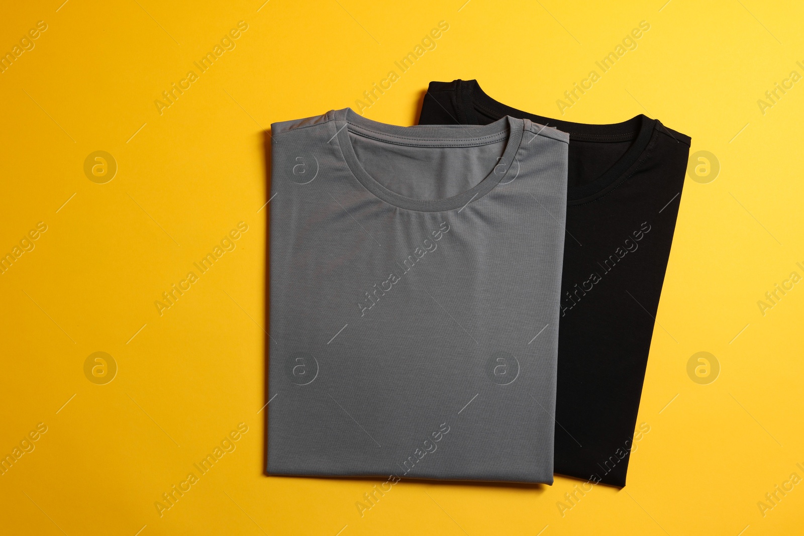 Photo of Different blank t-shirts on yellow background, top view. Mockup for design