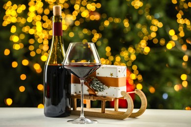 Photo of Glass and bottle of red wine with Christmas decor on table against blurred lights. Bokeh effect