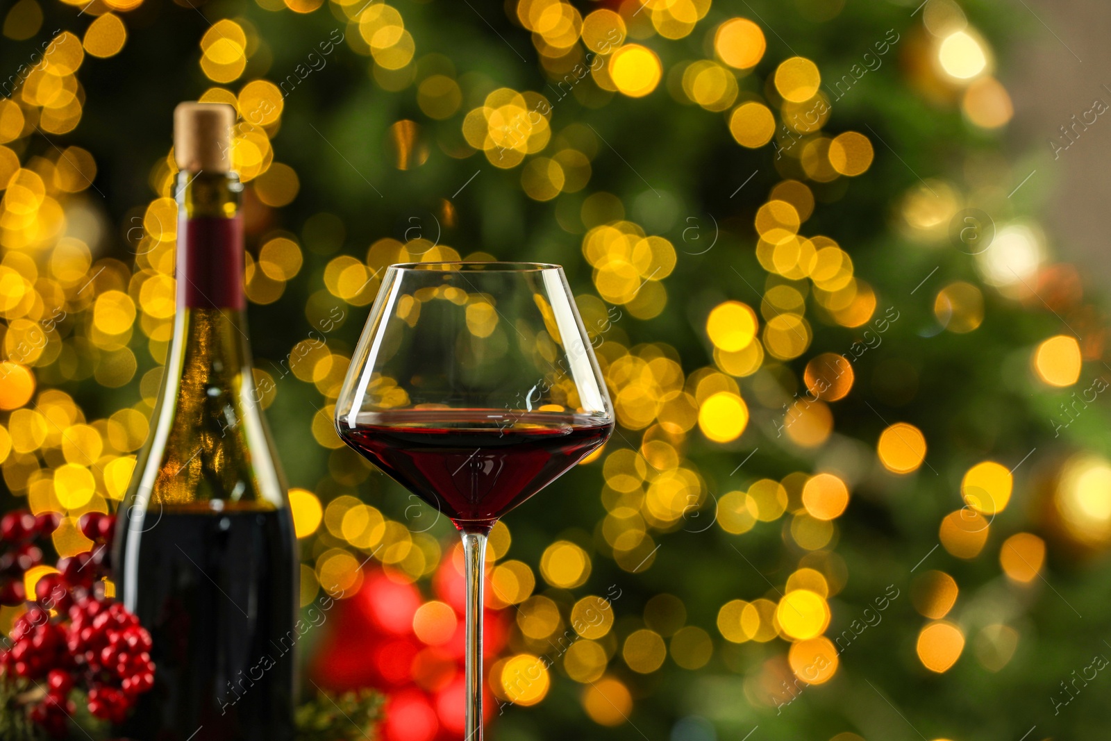 Photo of Bottle and glass of red wine against blurred Christmas lights, closeup with space for text. Bokeh effect