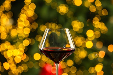 Glass of red wine against blurred Christmas lights, closeup. Bokeh effect