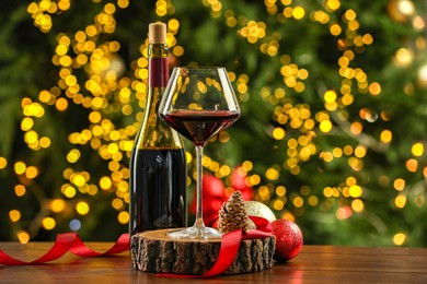 Photo of Glass and bottle of red wine with Christmas decor on wooden table against blurred lights. Bokeh effect