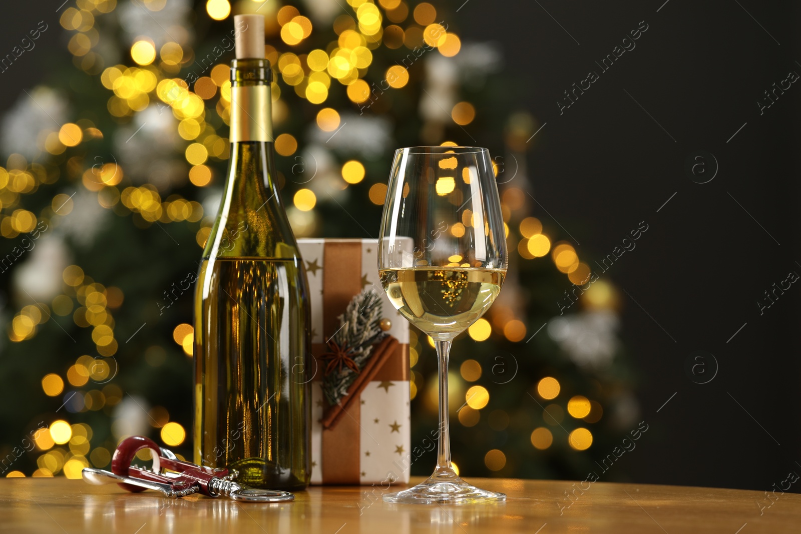 Photo of Wine in glass, bottle, wing corkscrew and Christmas gift on wooden table against blurred lights