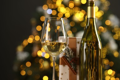 Photo of Wine in glass, bottle and Christmas gift against blurred lights, closeup