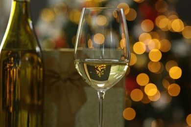 Photo of Wine in glass, bottle and Christmas gift against blurred lights, closeup